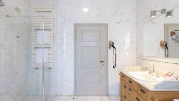 A bathroom with a glass shower enclosure, a white door, a vanity with a mirror, and a towel rack.