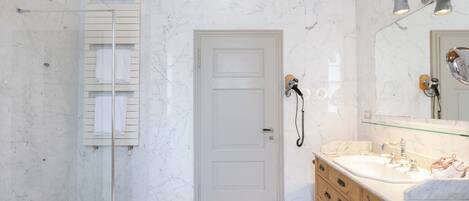 A bathroom with a glass shower enclosure, a white door, a vanity with a mirror, and a towel rack.