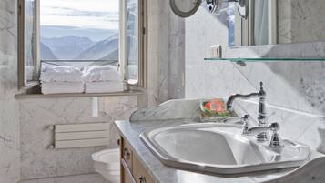 A bathroom with a large sink, wooden cabinets, a glass shelf, a mirror, and a window with a mountain view.