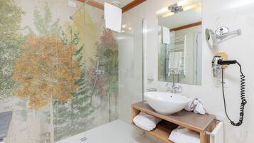 Une salle de bain avec une douche en verre, un lavabo blanc, un meuble-lavabo en bois et un miroir fixé au mur.