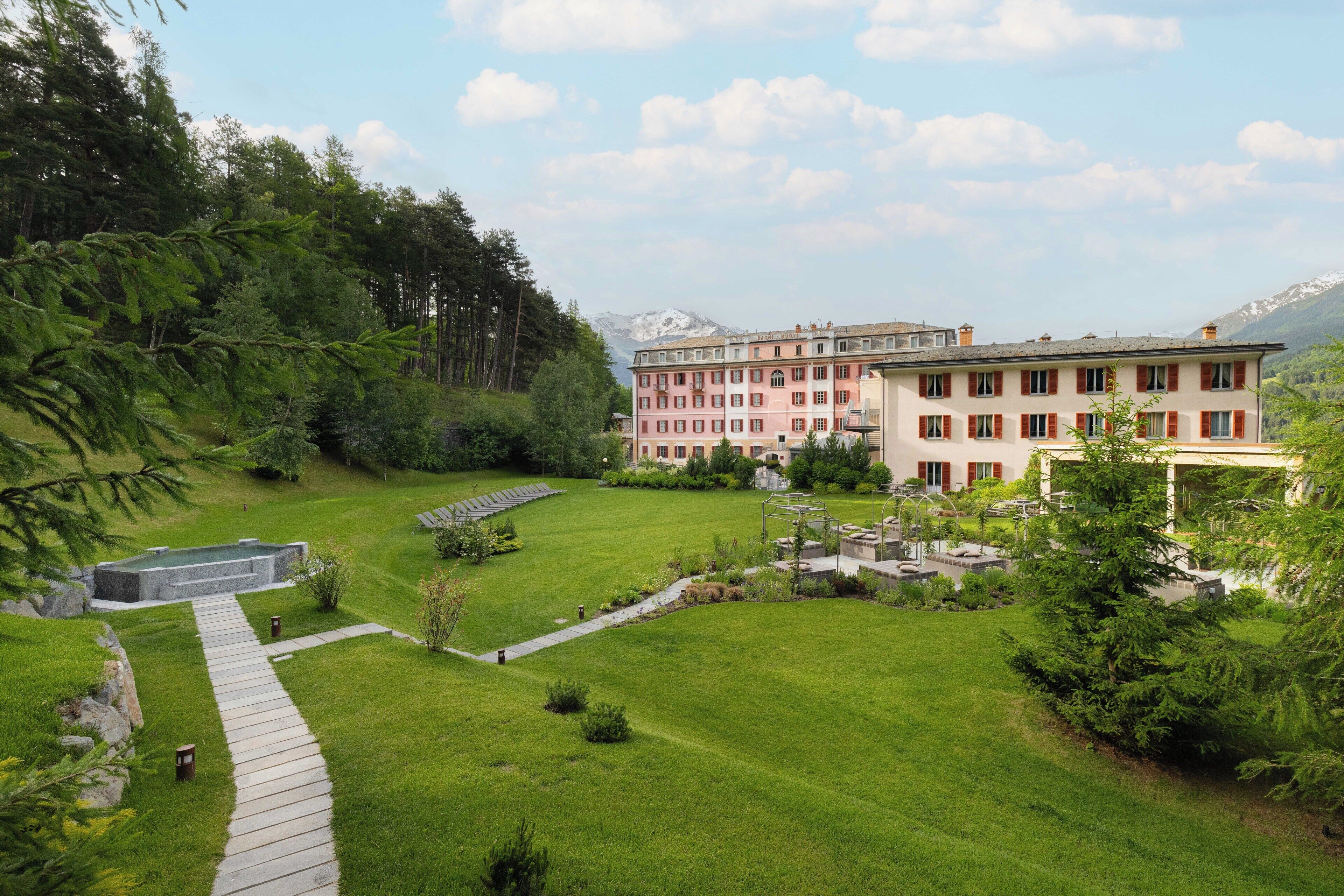 Ein Hotel mit gepflegter Rasenfläche, einem Kiesweg und Bergblick im Hintergrund.