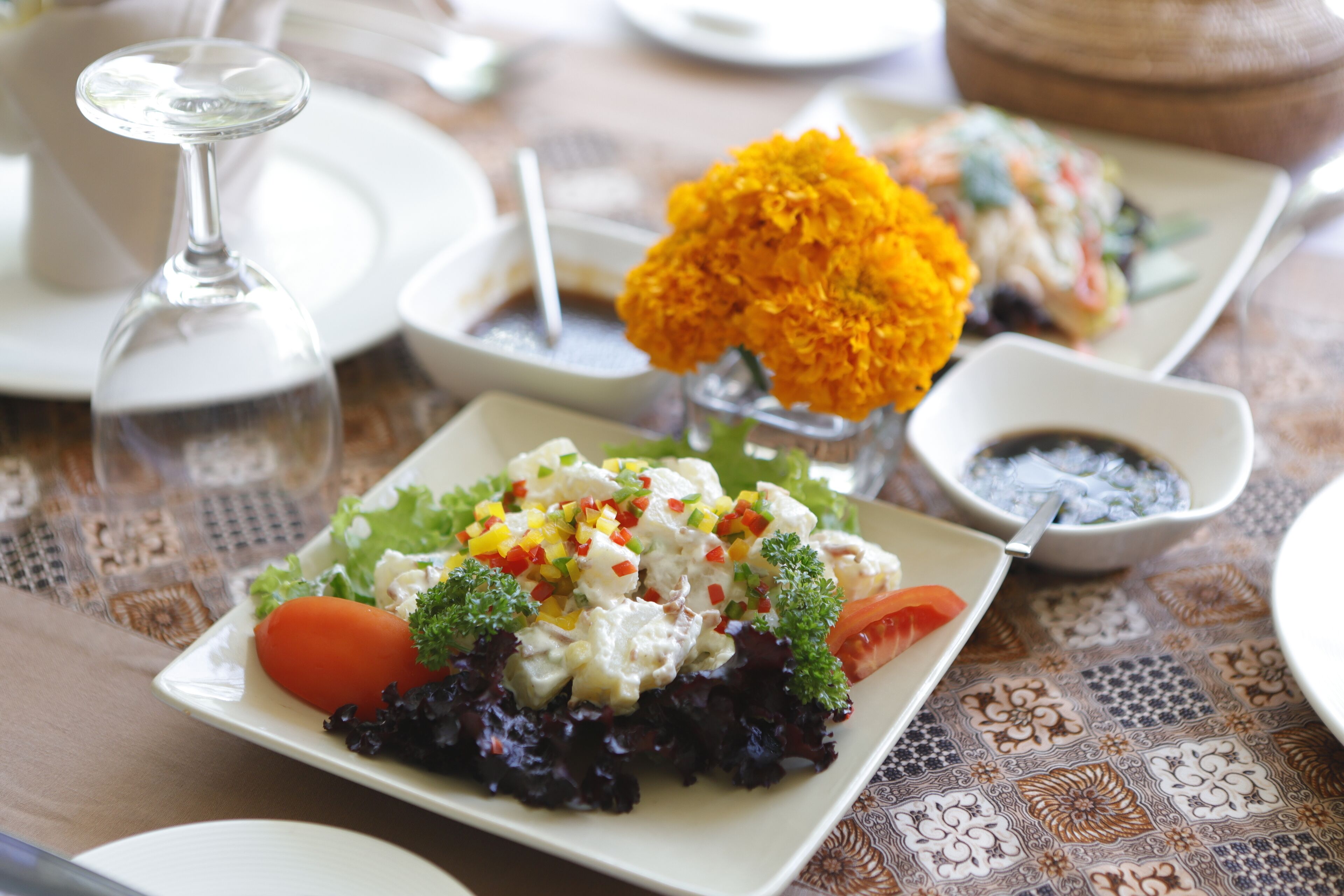 Una mesa puesta con platos de comida, un vaso de agua y un florero con flores.