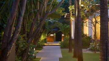 A pathway leading to a building with a gated entrance, surrounded by lush greenery and palm trees.