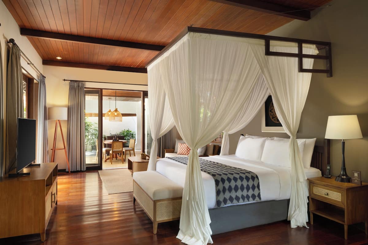A spacious bedroom with a large bed, a wooden ceiling, and a view of the outdoors.
