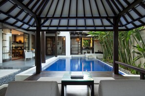 A modern outdoor pool area with a covered seating area and a view of the interior. - Alaya Dedaun Kuta (Legian)