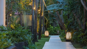 A pathway through a lush garden with palm trees and decorative lighting. - Alaya Dedaun Kuta (Legian)