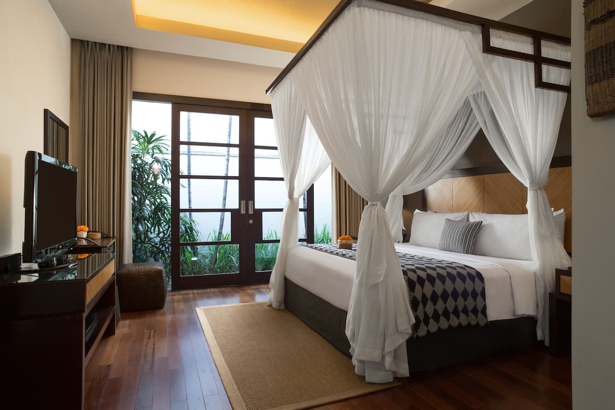 A bedroom with a four-poster bed, a television, and a view of greenery outside.