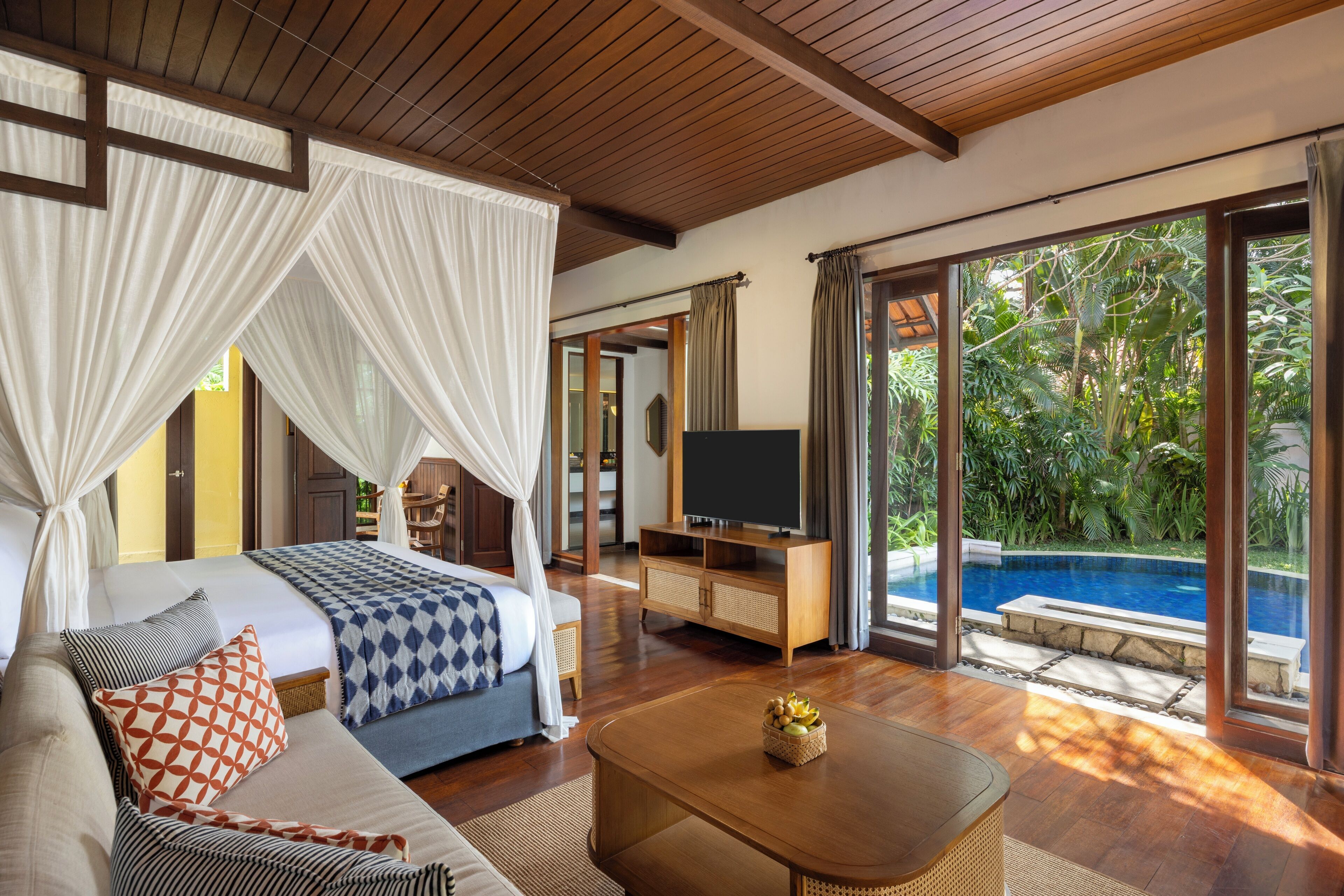 A bedroom with a bed, a TV, a coffee table, and a view of a swimming pool.