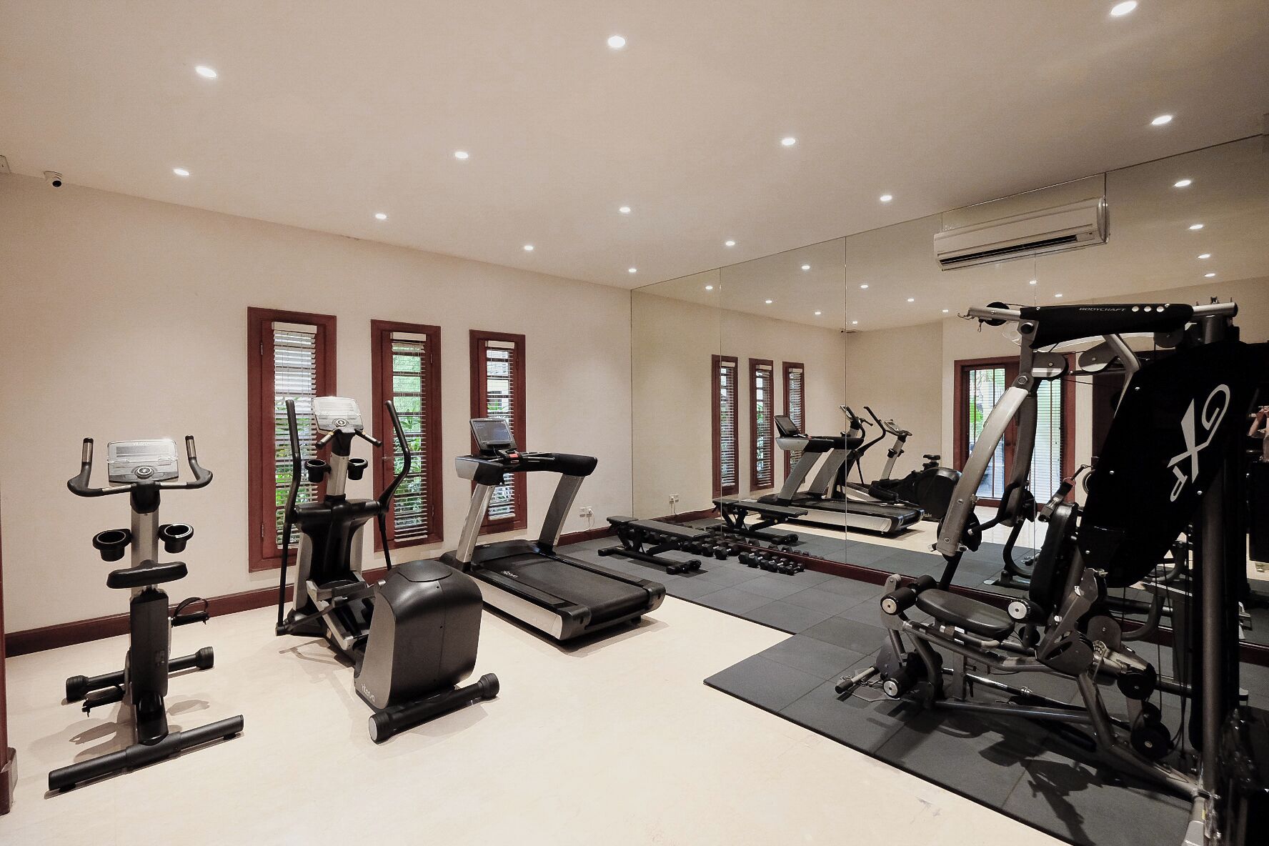 A well-equipped home gym with various exercise machines, including treadmills and a stationary bike, and a mirror reflecting the space.