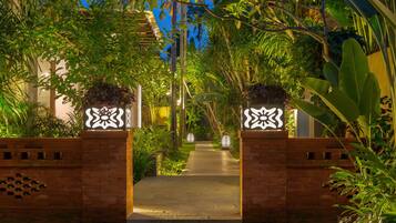 A pathway leading through a lush garden with a brick wall on one side and a white decorative gate on the other.