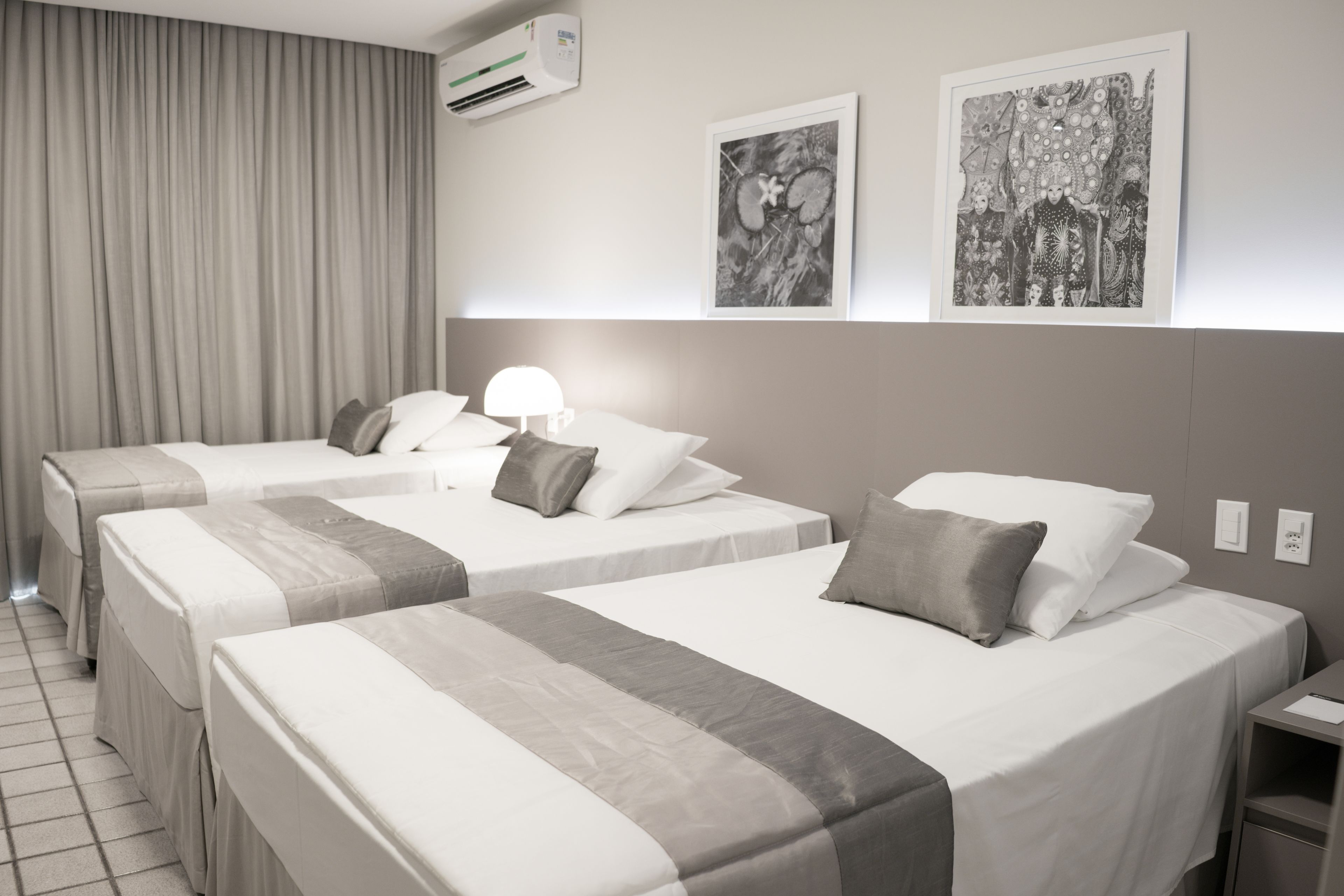 A hotel room with two beds, a nightstand, a lamp, and two framed artworks on the wall.