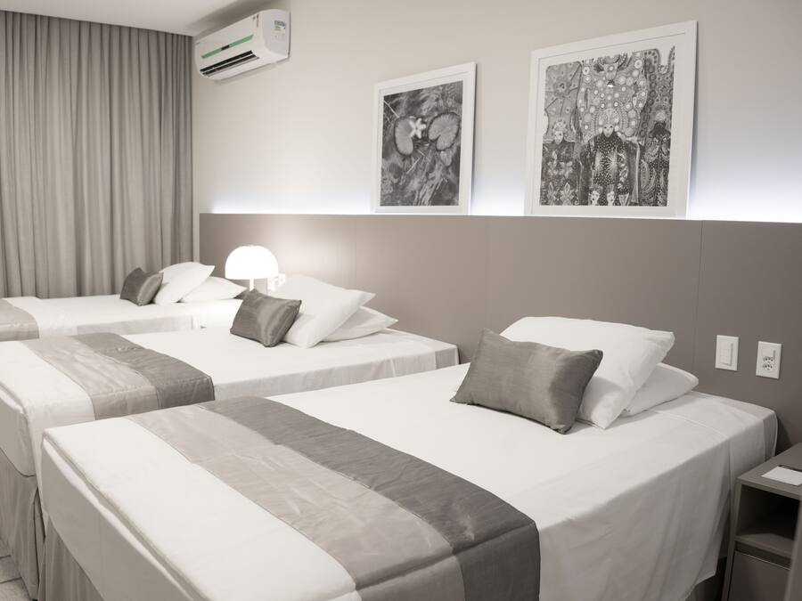 A hotel room with two beds, a nightstand, a lamp, and two framed artworks on the wall.
