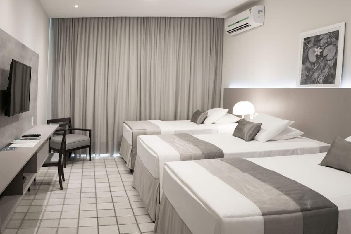 A hotel room with two beds, a desk, a chair, a TV, and a large window with curtains.