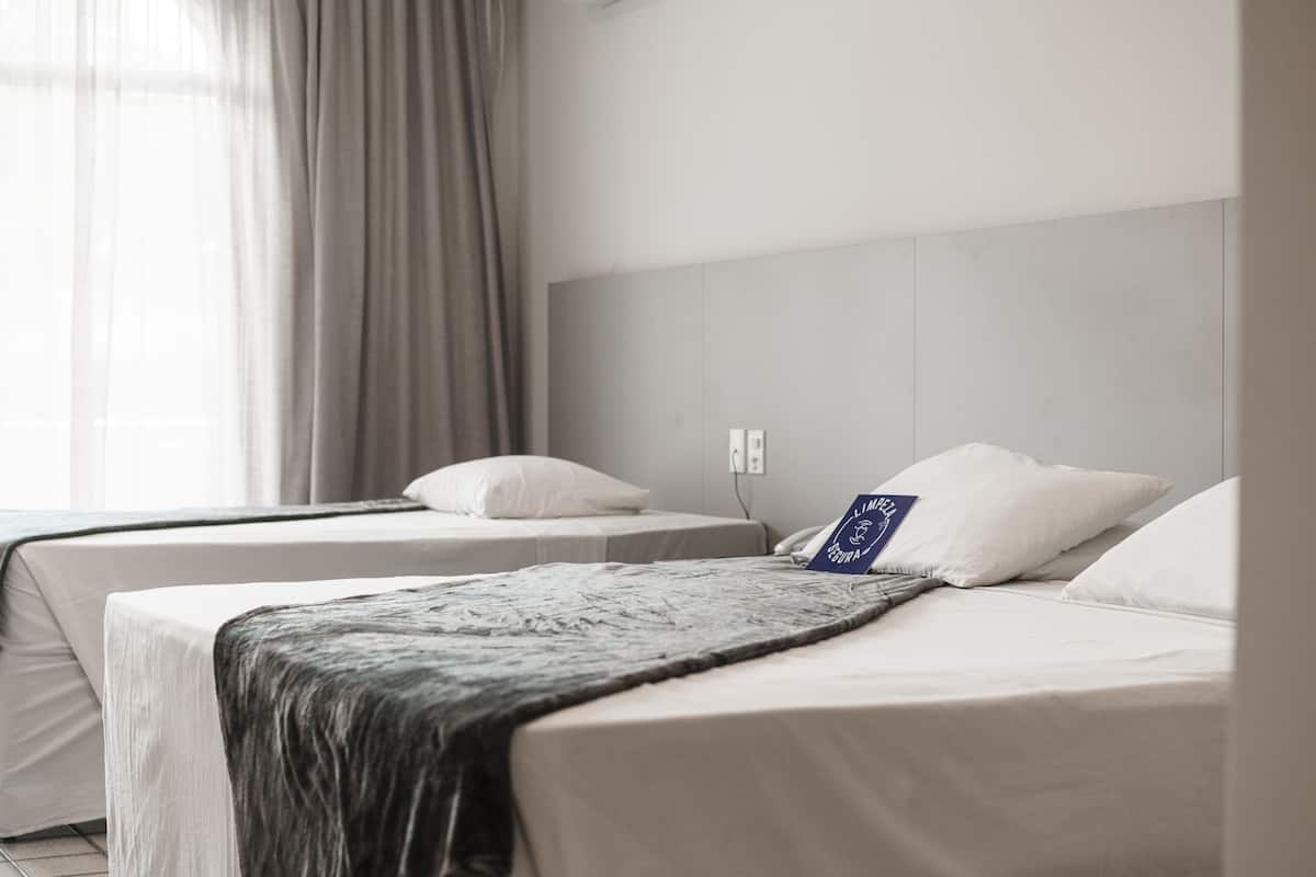 A hotel room with two beds, a large window with curtains, and a wall-mounted phone.