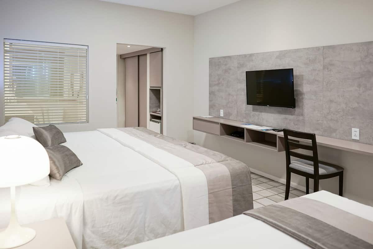 A hotel room with a bed, a desk, a chair, a TV, and a window with blinds.