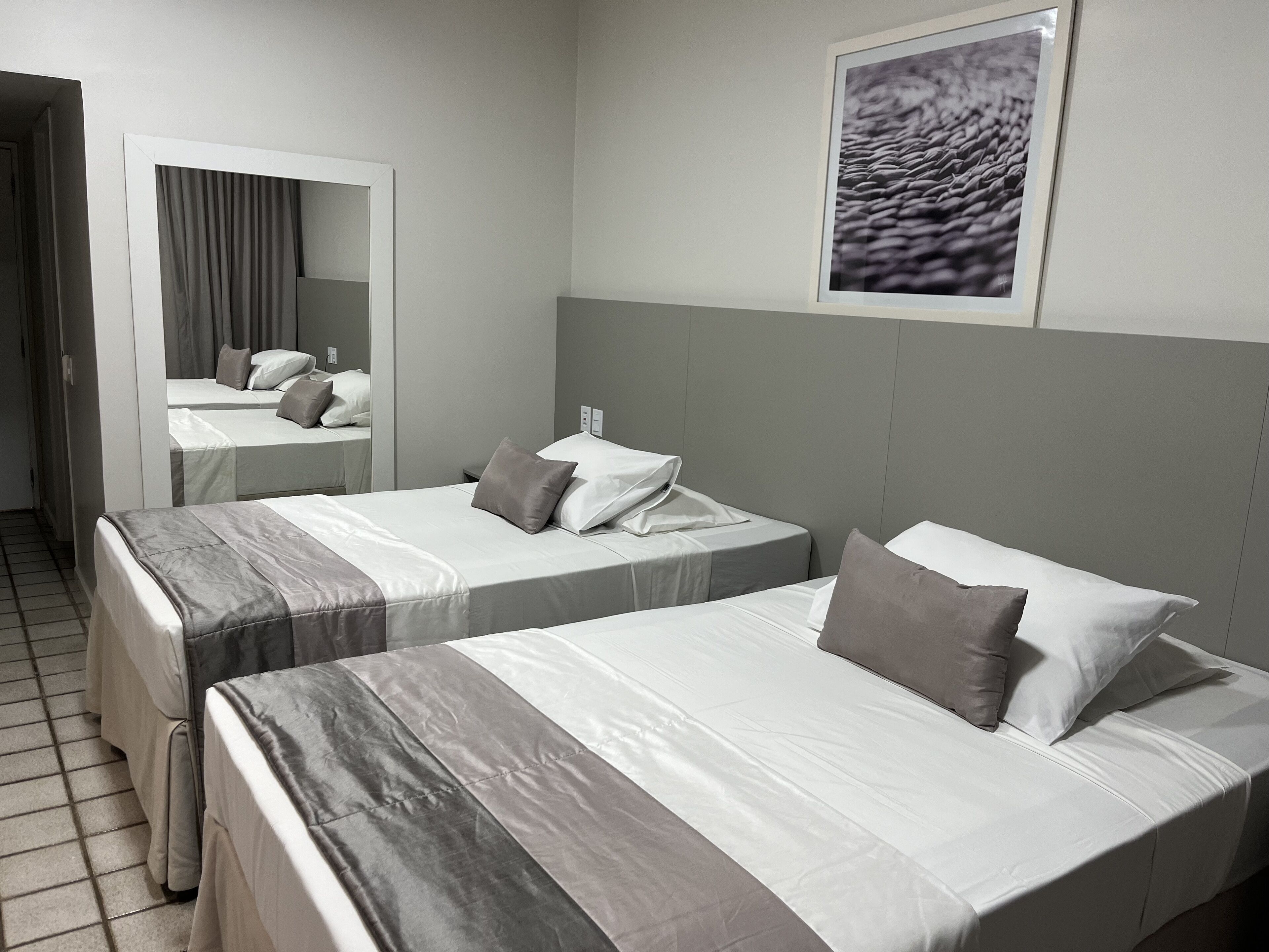 Ein Hotelzimmer mit zwei Betten, einem Spiegel und einem gerahmten Bild an der Wand.