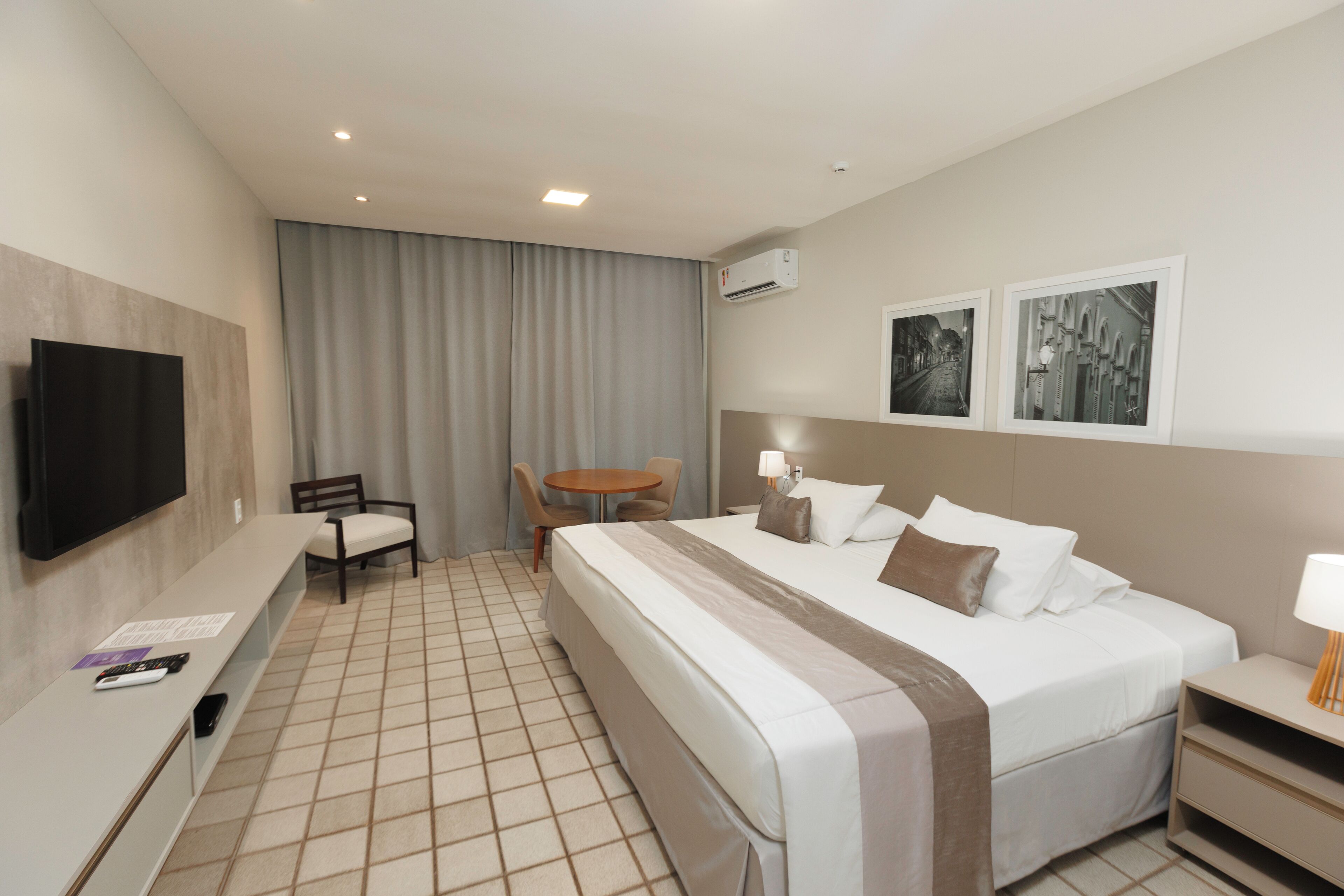 Une chambre d’hôtel avec un lit, un bureau, une chaise, une télévision et deux tableaux encadrés au mur.
