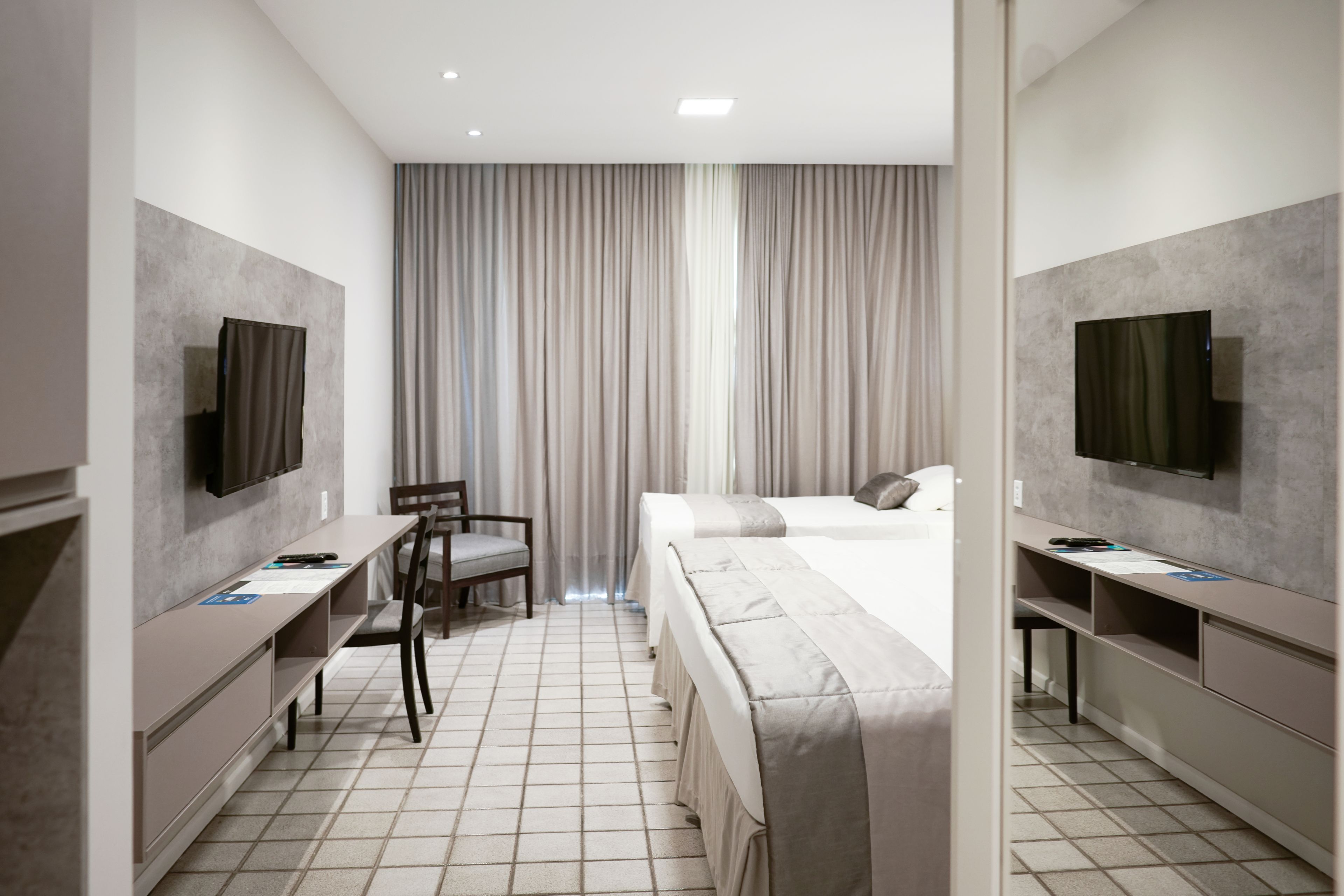 A modern hotel room with a bed, a desk, a chair, a TV, and a large window with curtains.