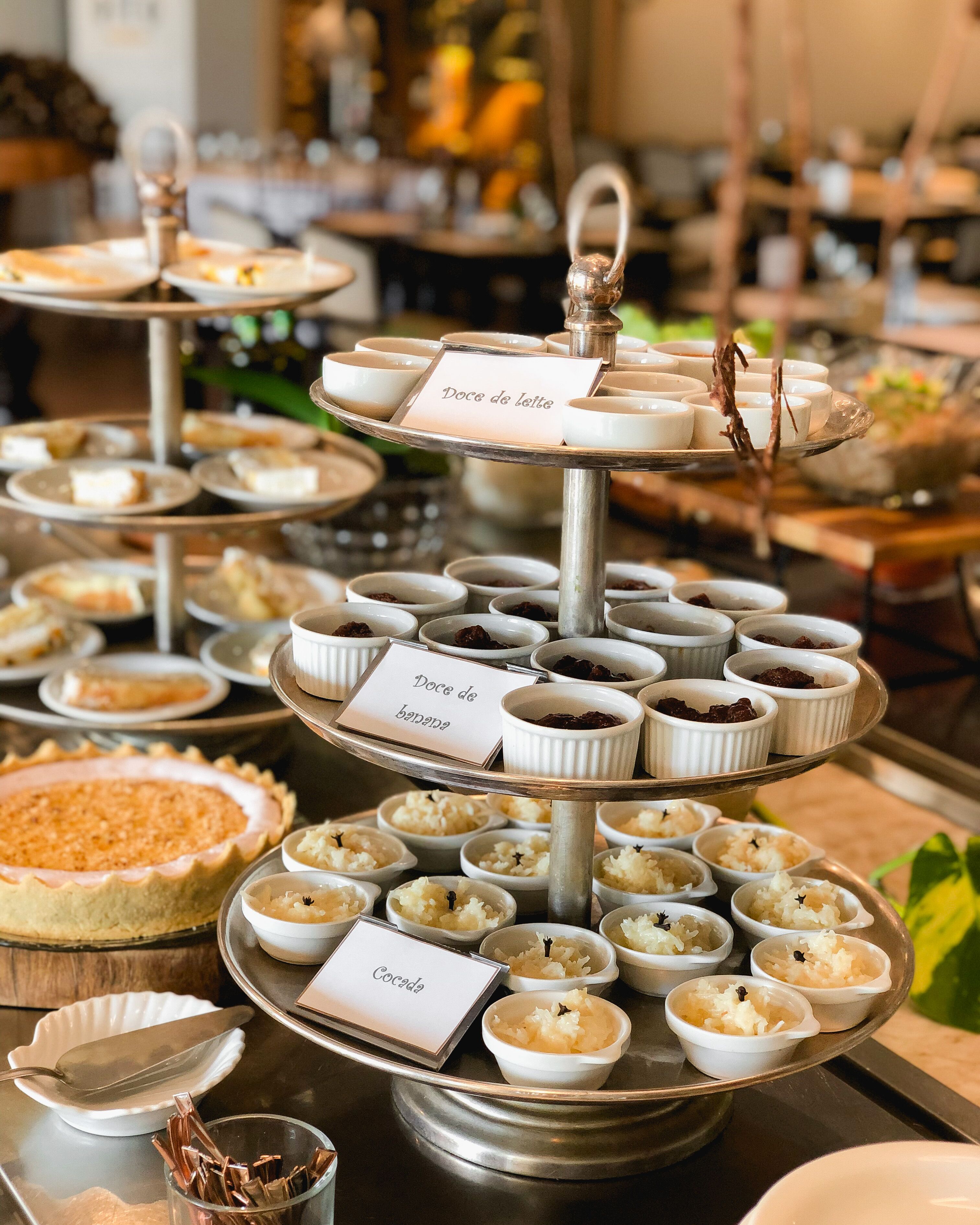 Un buffet proposant une grande variété de desserts, présentés sur différents plateaux, avec des étiquettes indiquant leur nom, comme « Doce de leite » et « Doce de banana ».