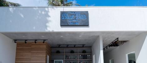 A bar named "Blue Bar" with a wooden counter and shelves of bottles.