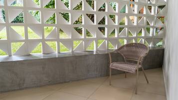 Una habitación con un banco de concreto, una silla de mimbre y un panel de celosía blanca con aberturas triangulares.