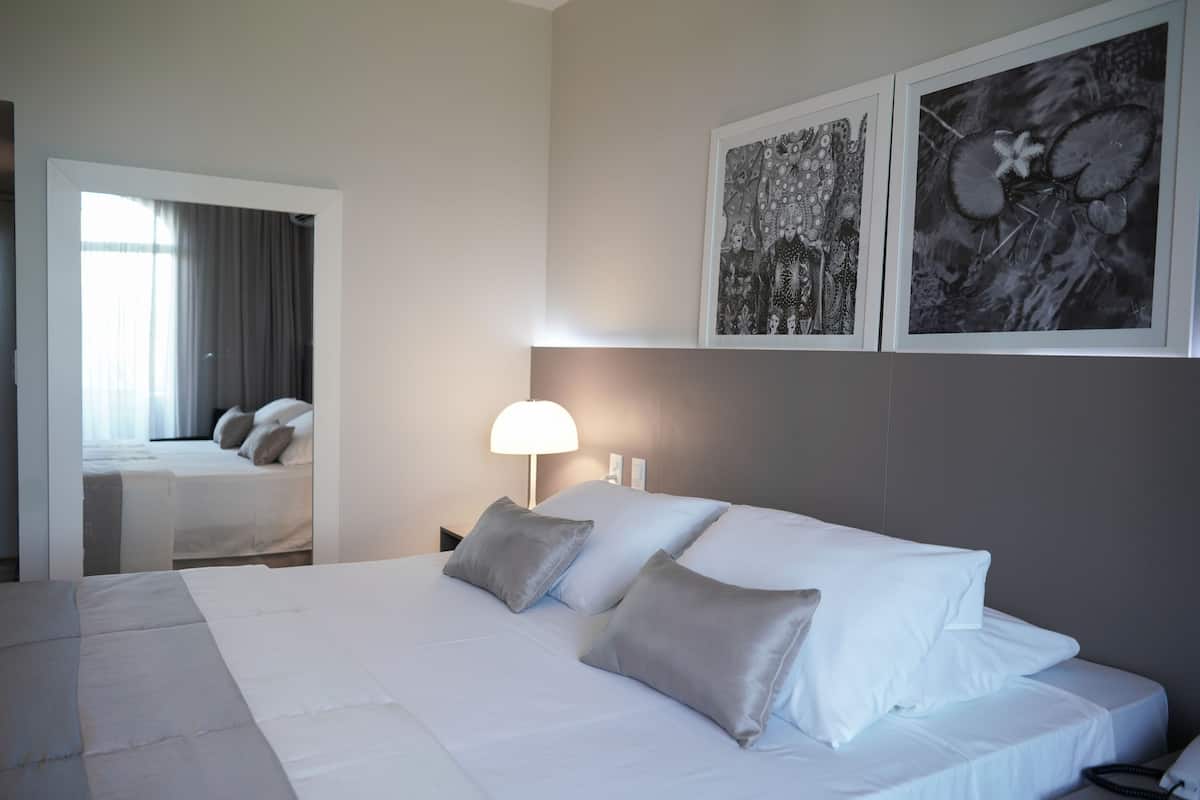 A hotel room with a bed, a nightstand, a lamp, and two framed pictures on the wall.