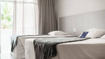 A hotel room with two beds, a large window with sheer curtains, and an air conditioning unit on the wall.