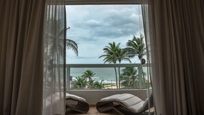 Un balcón con dos sillones de descanso, vista al océano, palmeras y un cielo nublado.