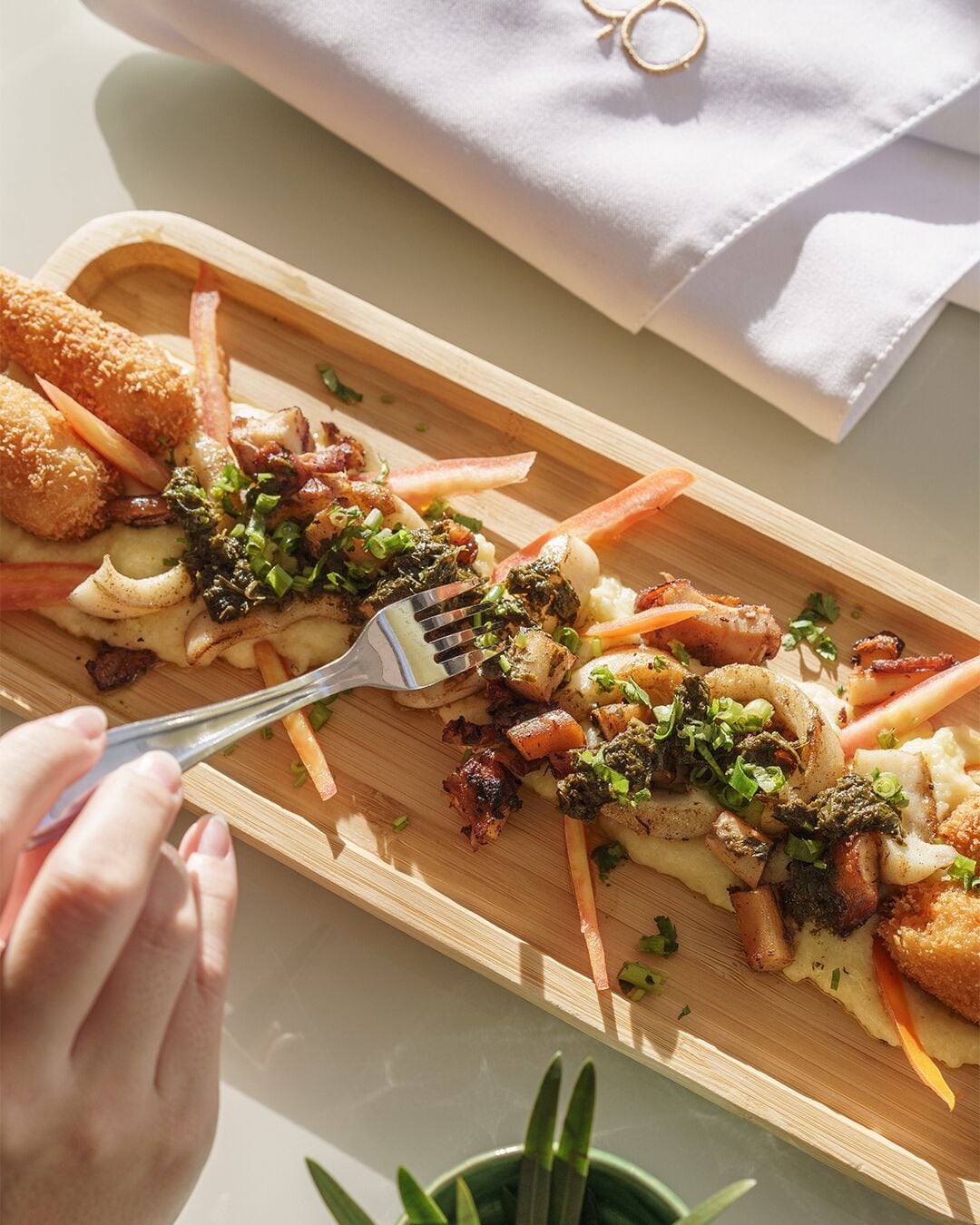 A wooden serving board with a variety of food items, including what appears to be a breaded cutlet, vegetables, and a sauce.