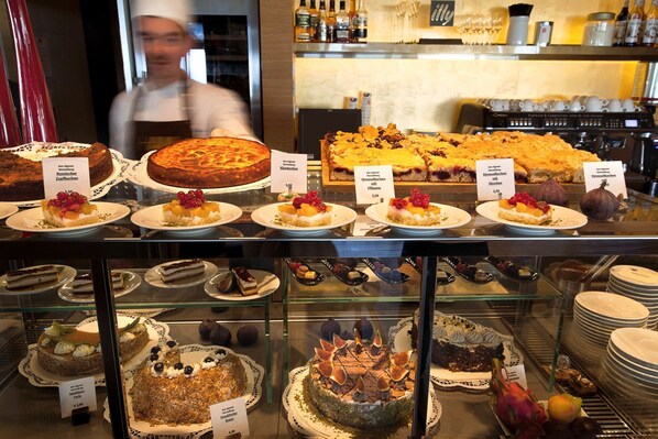 A bakery display with various cakes and pastries, including a large round cake and several smaller ones with fruit toppings. - Hotel Am Meer & Spa (Binz)
