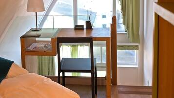 A bedroom with a bed, a desk with a lamp, a chair, and a window with curtains.