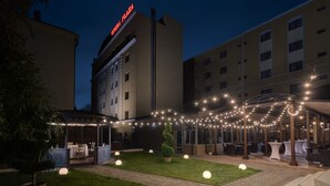 Un espacio al aire libre con un conjunto de asientos, una zona cubierta y un edificio con un letrero que dice "OPERA PLAZA".