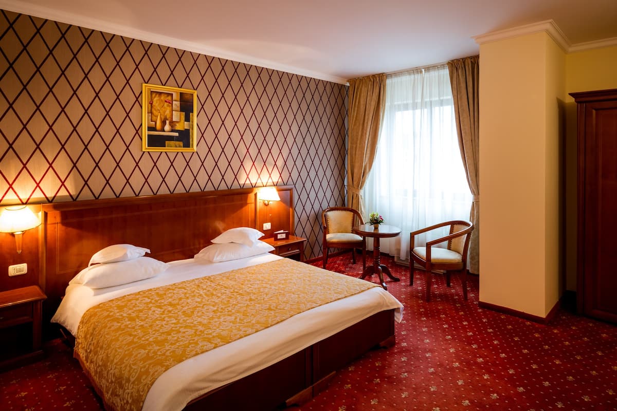A hotel room with a large bed, two bedside tables, a desk, a chair, and a window with curtains.