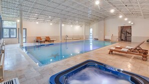 Una piscina interior con hidromasaje, sillones de descanso y vistas al exterior.
