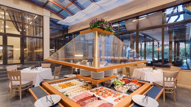 Disposición de bufé con diferentes opciones de comida, una vitrina de vidrio y vistas al exterior a través de amplias ventanas.