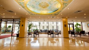 Un hall espacioso con techo decorativo, ventanas amplias y una alfombra roja que conduce a la entrada.