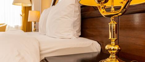 A neatly made bed with white linens, a gold-plated lamp on a wooden nightstand, and a wooden headboard.