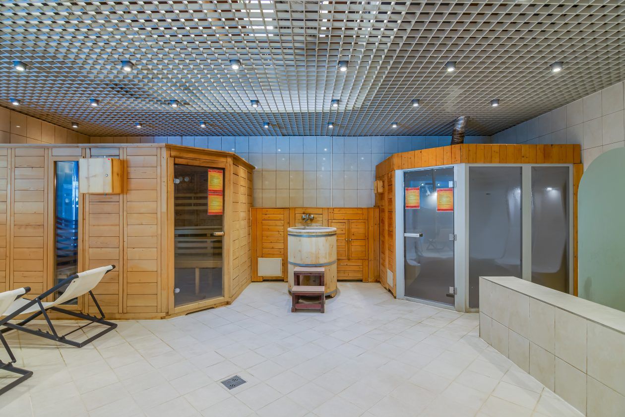 A sauna room with wooden walls, a wooden bench, a sauna tub, and a glass door.