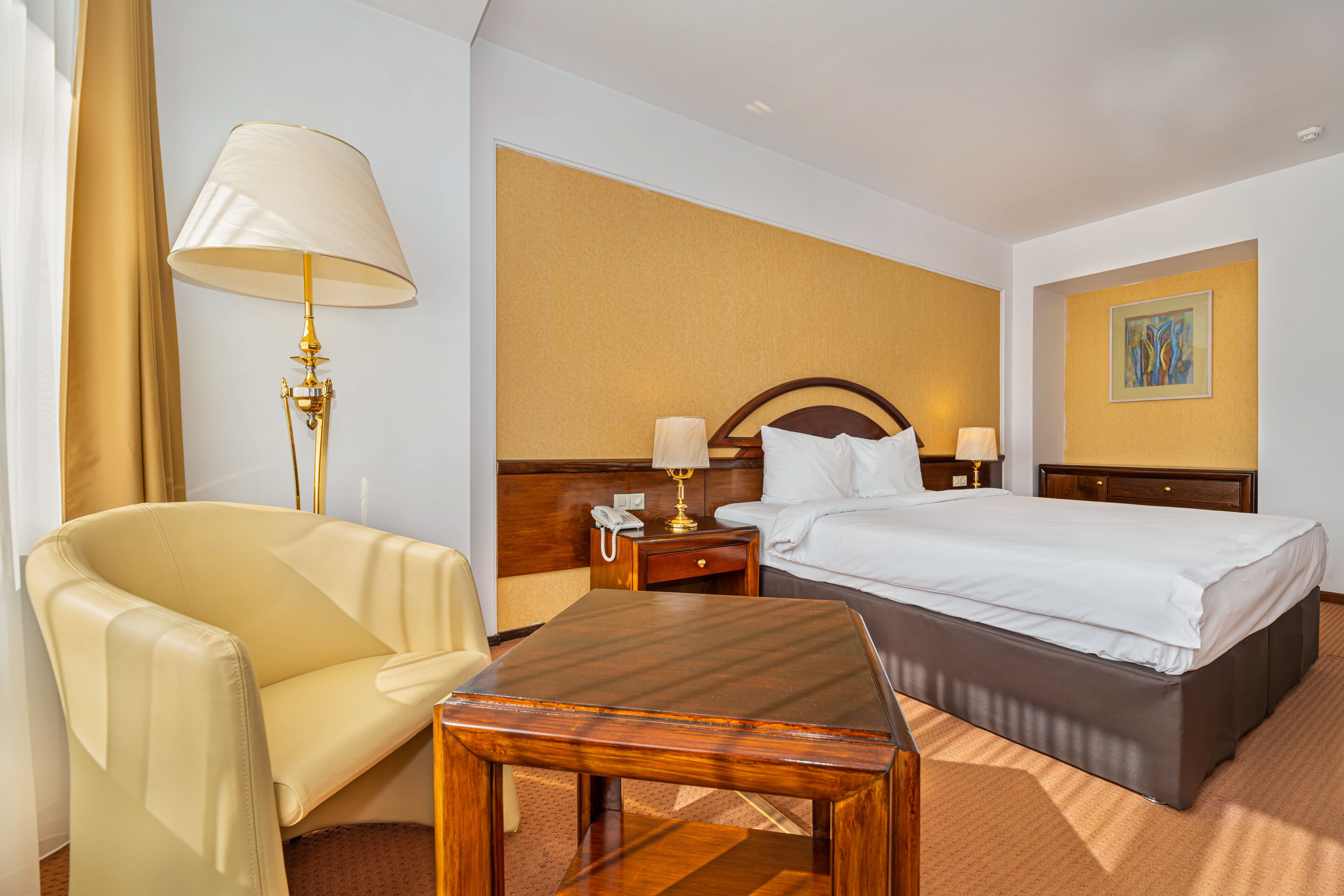 A hotel room with a bed, a desk, a chair, a lamp, and a nightstand.