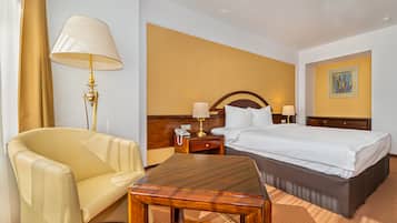 Una habitación de hotel con cama, escritorio, silla, lámpara y mesita de noche.