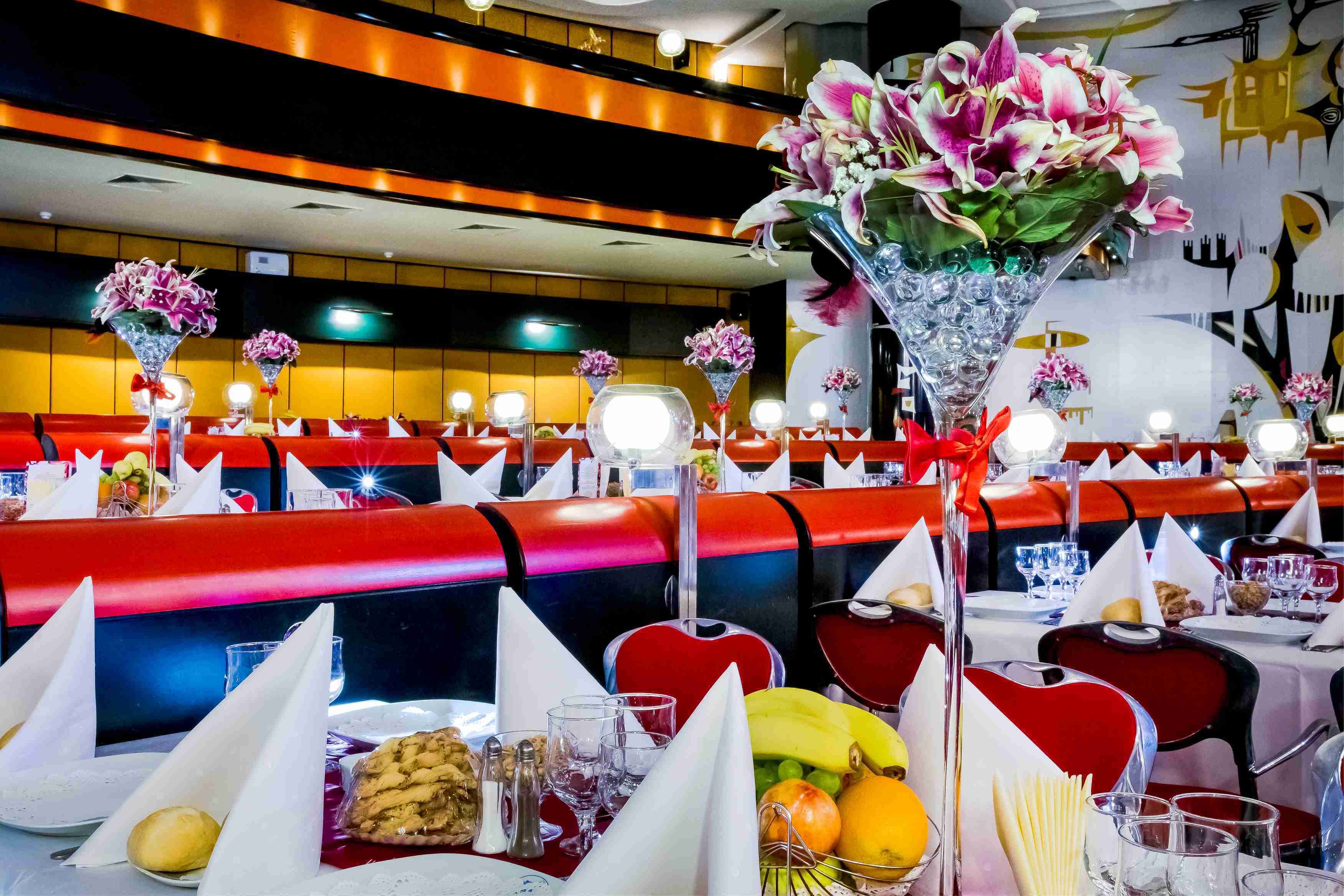 A restaurant with red booths, white tablecloths, and floral centerpieces.