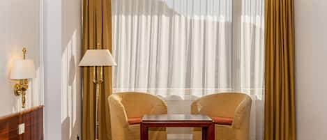 Habitación de hotel con una cama, dos sillones, una mesita, una lámpara y cortinas traslúcidas.