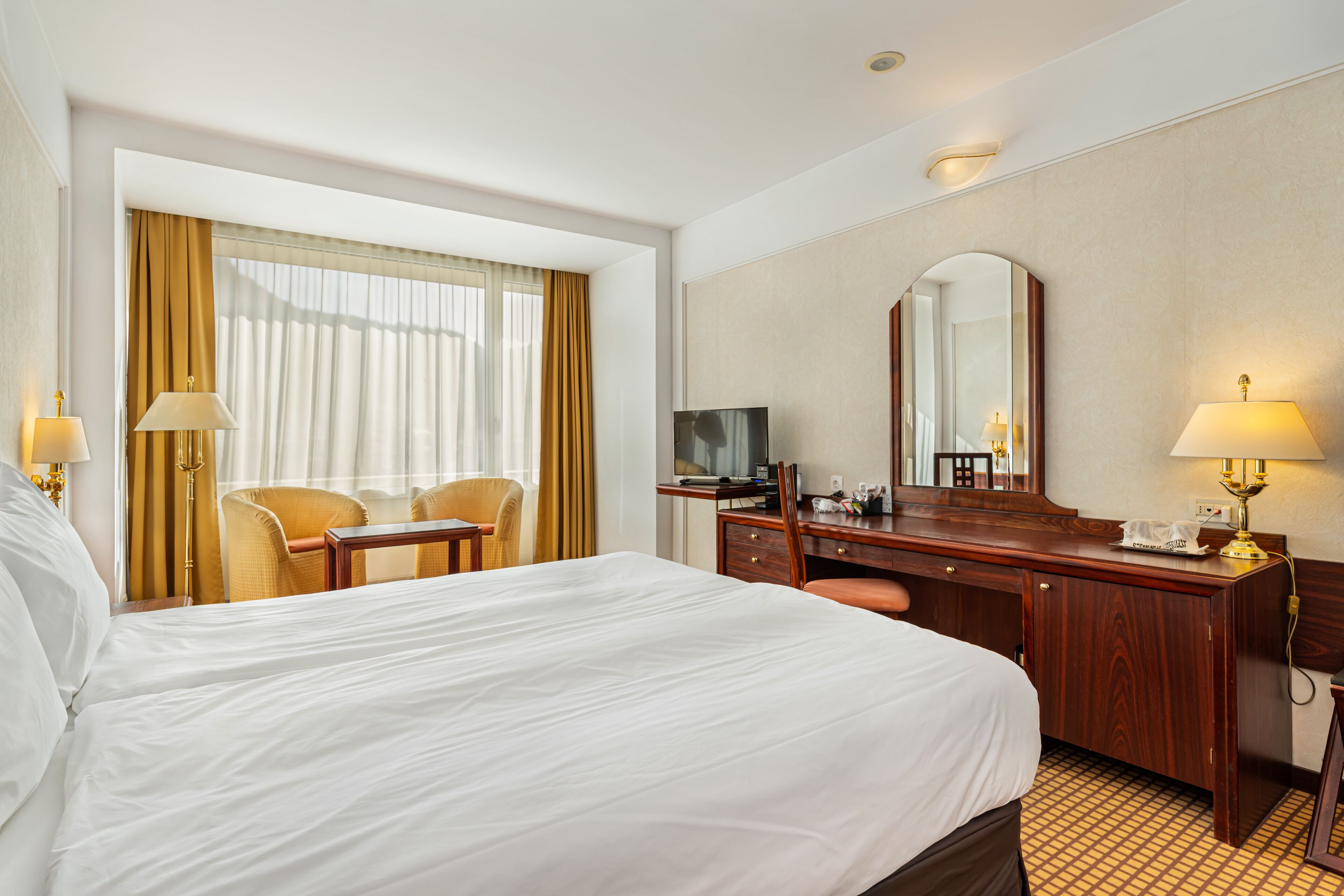 Una habitación de hotel con una cama grande, un escritorio con espejo, televisión y una silla.