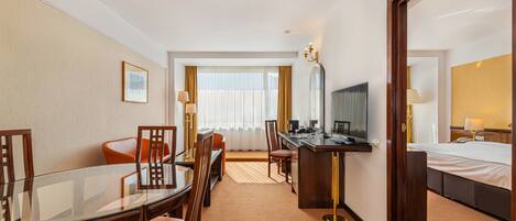 Habitación de hotel con mesa de comedor, sillas, escritorio, cama y un espejo grande.
