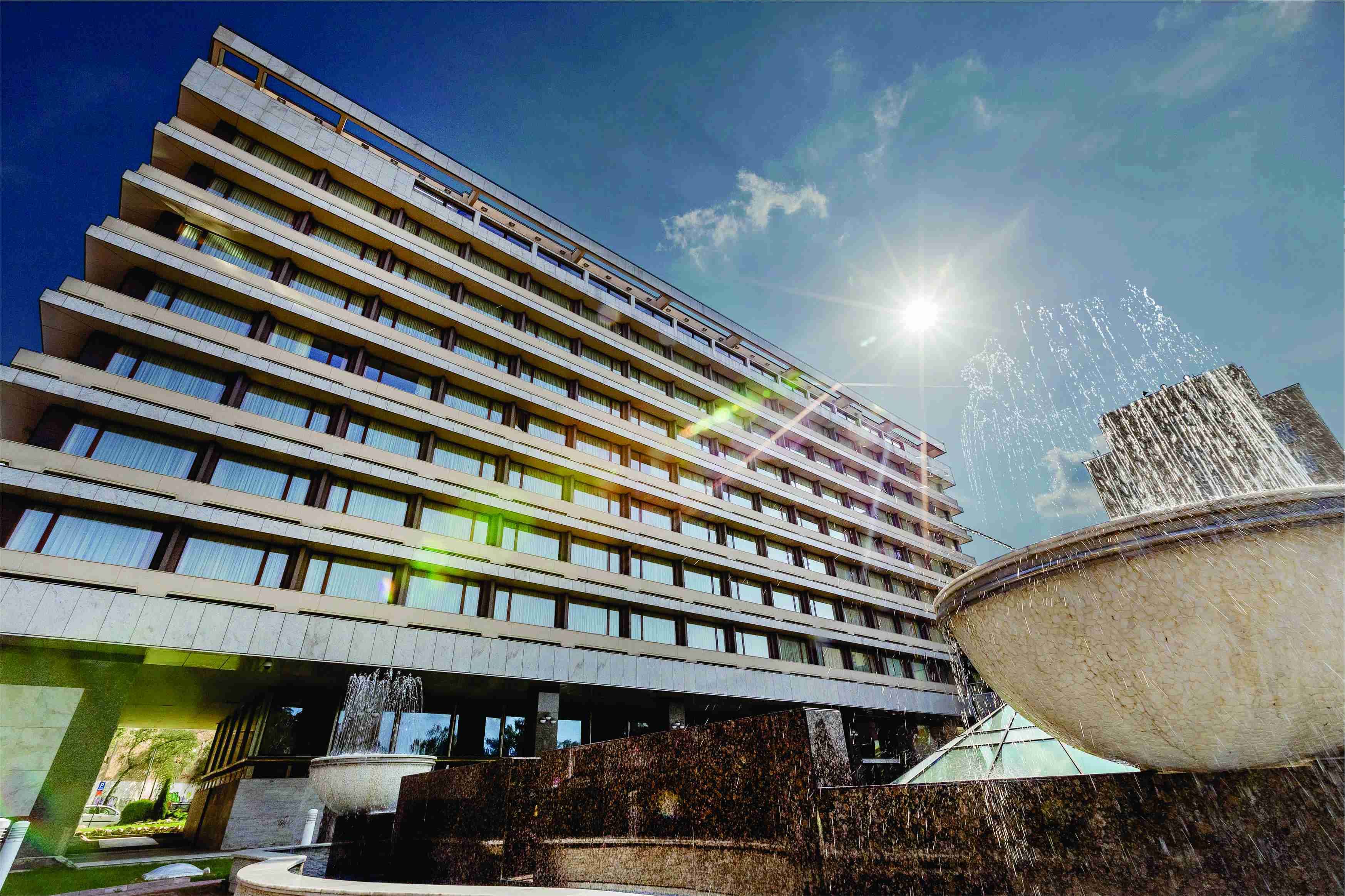 A modern hotel with a multi-story structure, a central courtyard with a fountain, and a large reflective pool.