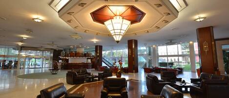 A spacious lobby with leather seating, a central chandelier, and large windows offering a view of the outdoors.