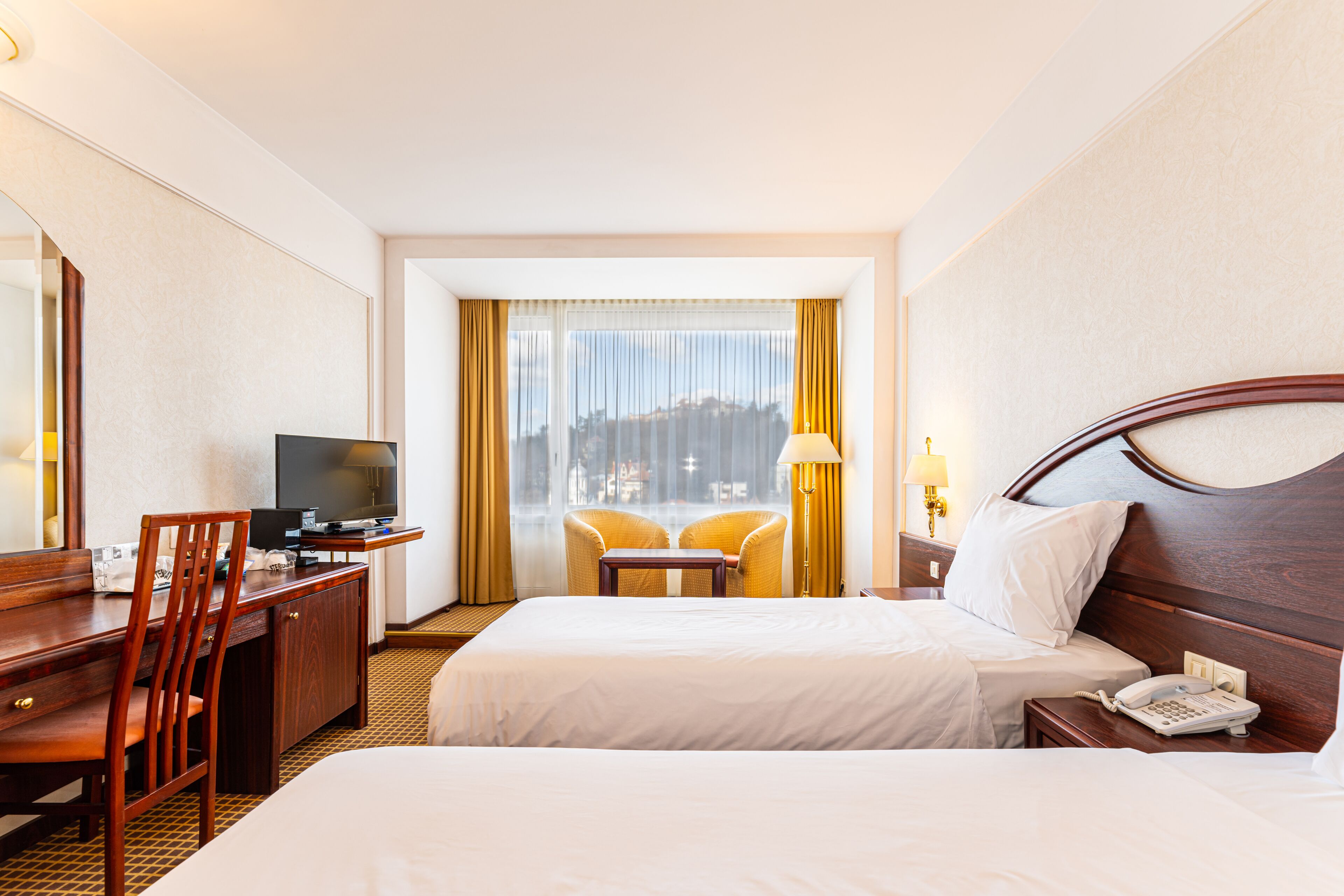 A hotel room with two beds, a desk with a TV, a chair, and a window with curtains.