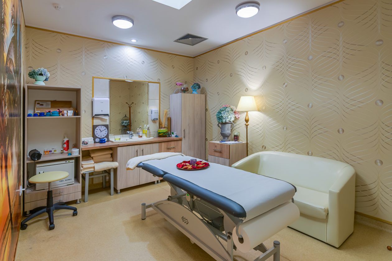 Un consultorio médico con una cama, mesa de exploración y un escritorio con material médico.