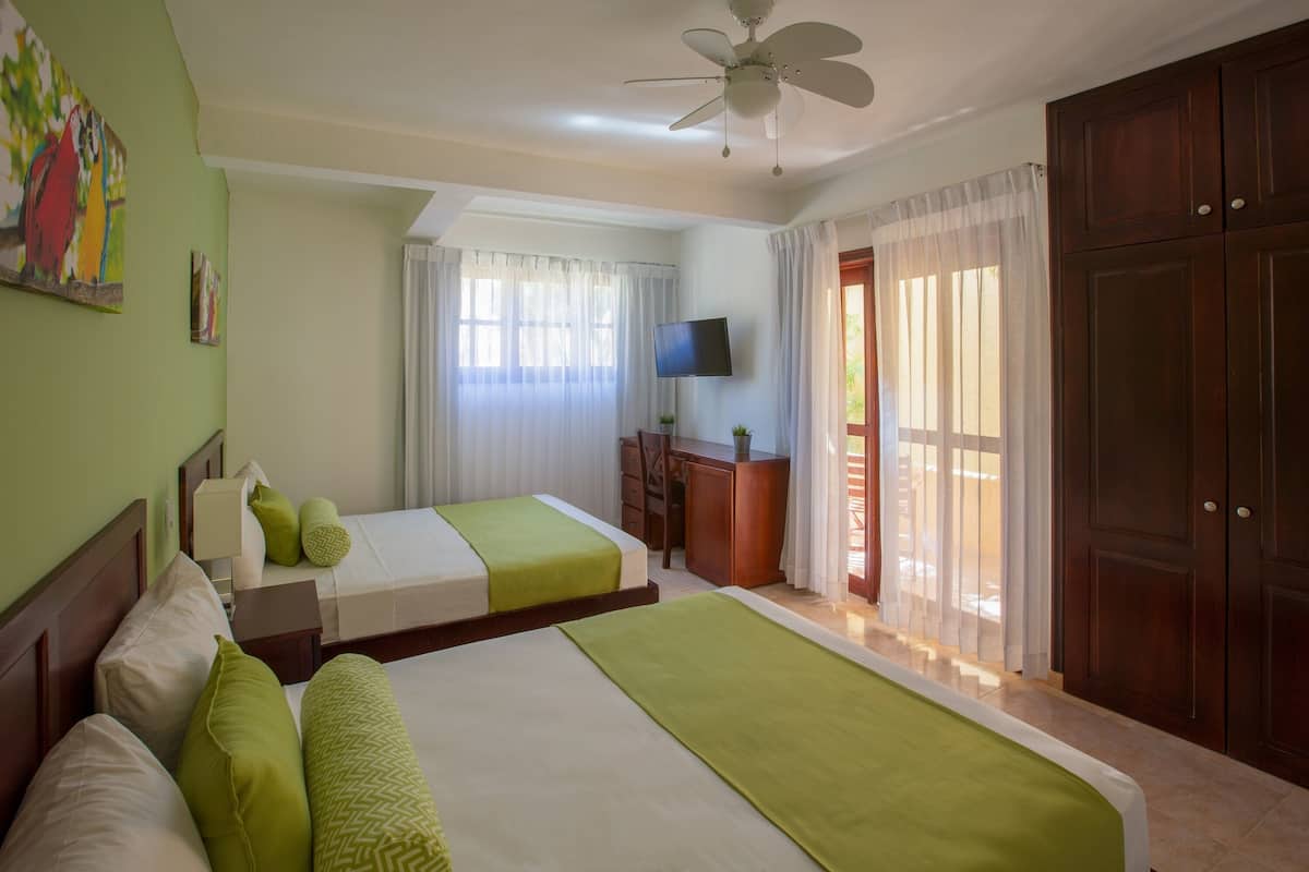 A hotel room with two beds, a desk, a TV, and a large wardrobe.