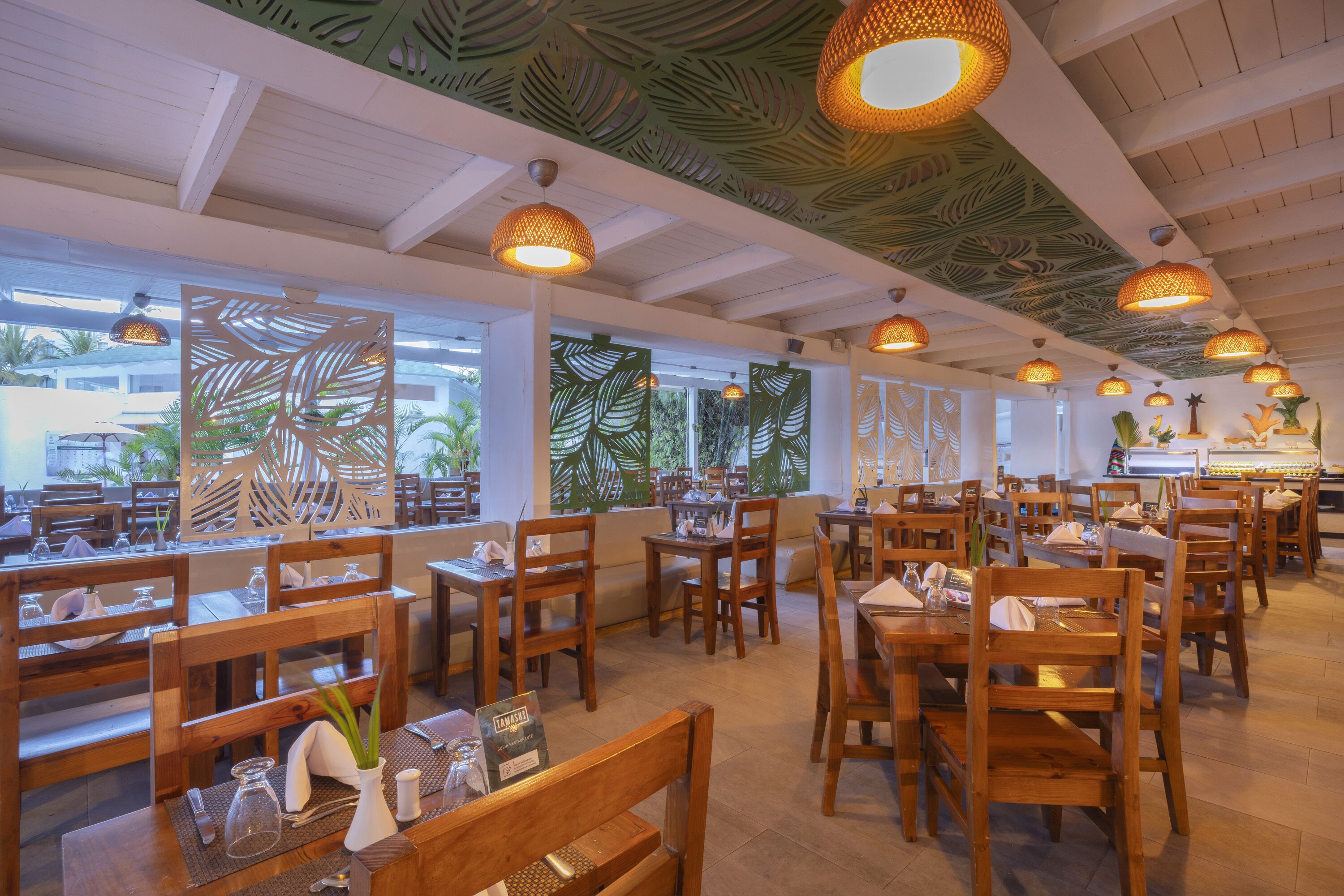 A restaurant with wooden tables and chairs, large windows, and a ceiling with a leaf pattern.